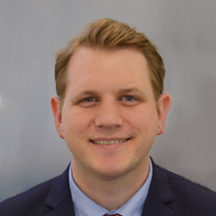 Headshot of Jon Brumbach against grey background.