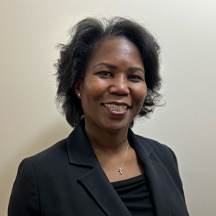 Randi Moberly, a woman with shoulder-length dark hair, wearing a black blazer and a black top, smiles at the camera. She is standing against a plain, light-colored background.